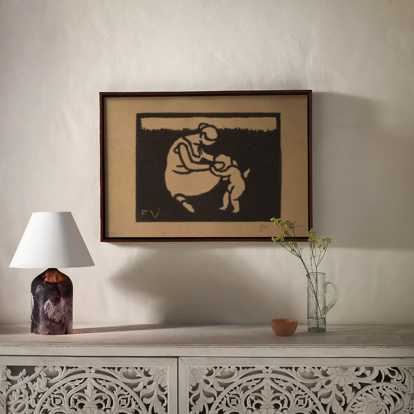 Framed artwork on a wall above a decorative console table with a lamp and vase.