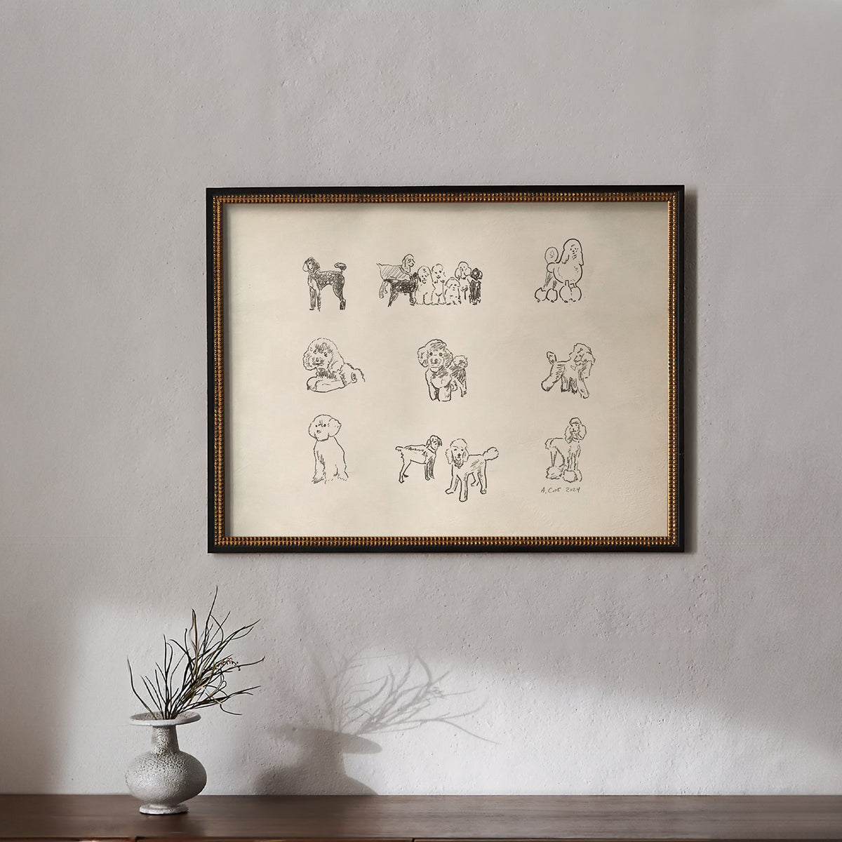 Framed artwork with illustrations of dogs on a beige background, displayed on a wall above a wooden surface.