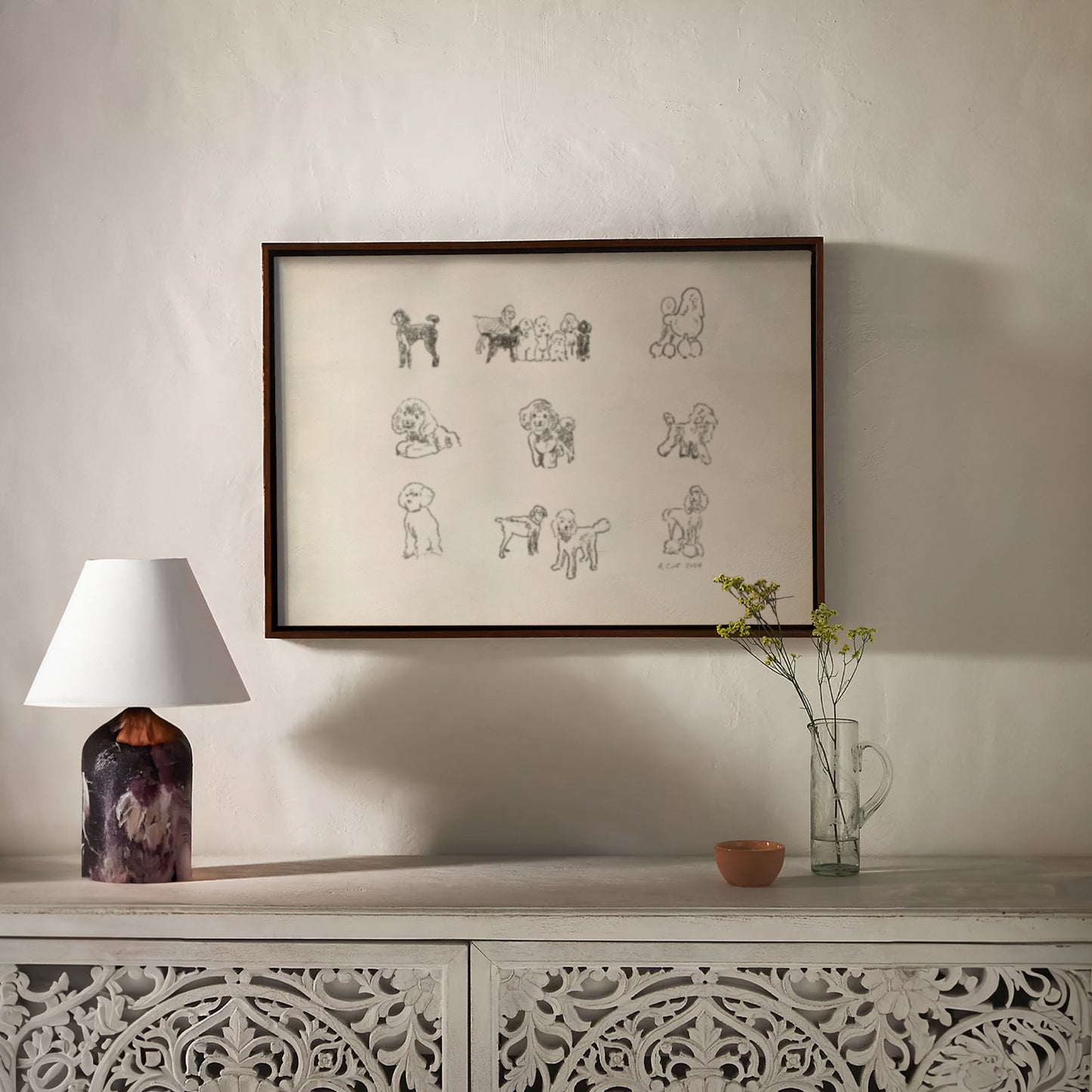 Framed artwork on a wall above a decorative console table with a lamp and vase.