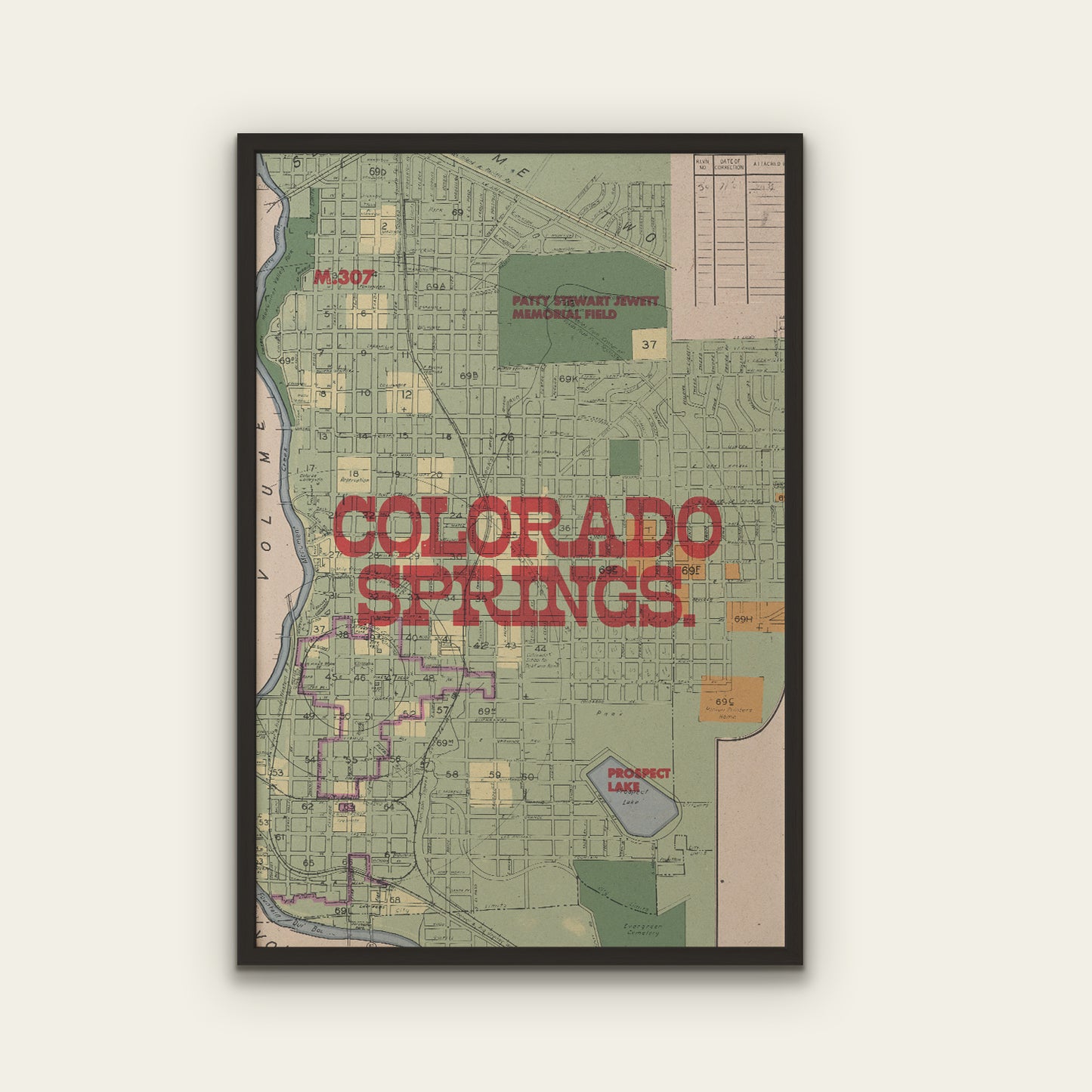 A framed vintage-style map print of Colorado Springs, Colorado, featuring a muted green street grid, red 'COLORADO SPRINGS' lettering, and a black frame against a light beige wall.