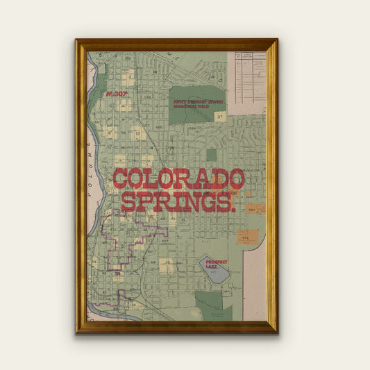 Framed vintage-style map wall art of Colorado Springs, featuring a gold frame, muted street map details, and large red text reading 'COLORADO SPRINGS' on a light beige background.