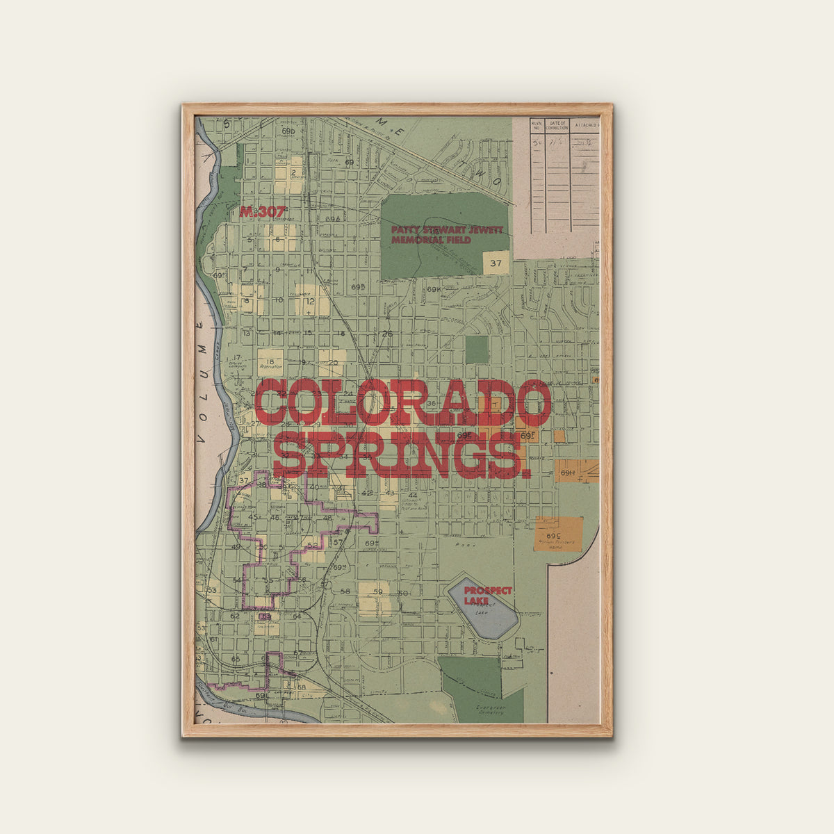 A framed vintage-style map print of Colorado Springs, Colorado, featuring a light wood frame and bold red text reading 'COLORADO SPRINGS' across the center, shown against a plain light beige background.