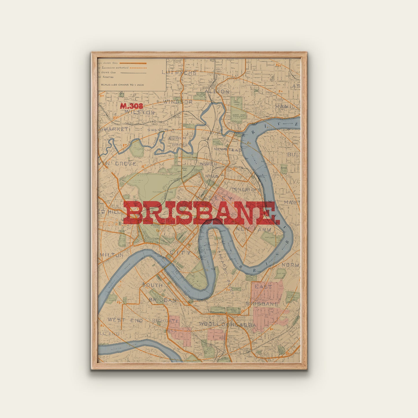 A framed vintage-style map print of Brisbane, Australia, with the city name in large red letters across the center. The map shows the river winding through the city in muted blue and green tones, with a light wood frame, displayed against a plain light beige wall.