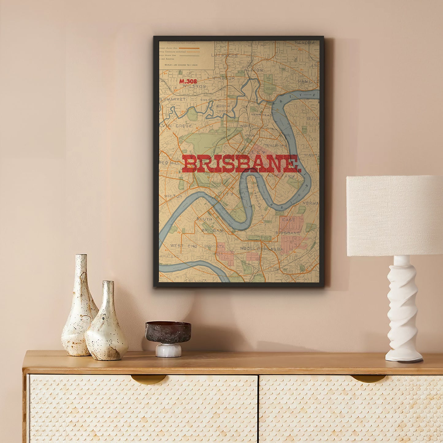 A framed vintage-style Brisbane map print hangs on a beige wall above a wooden console table with decorative vases, a bowl, and a white lamp.