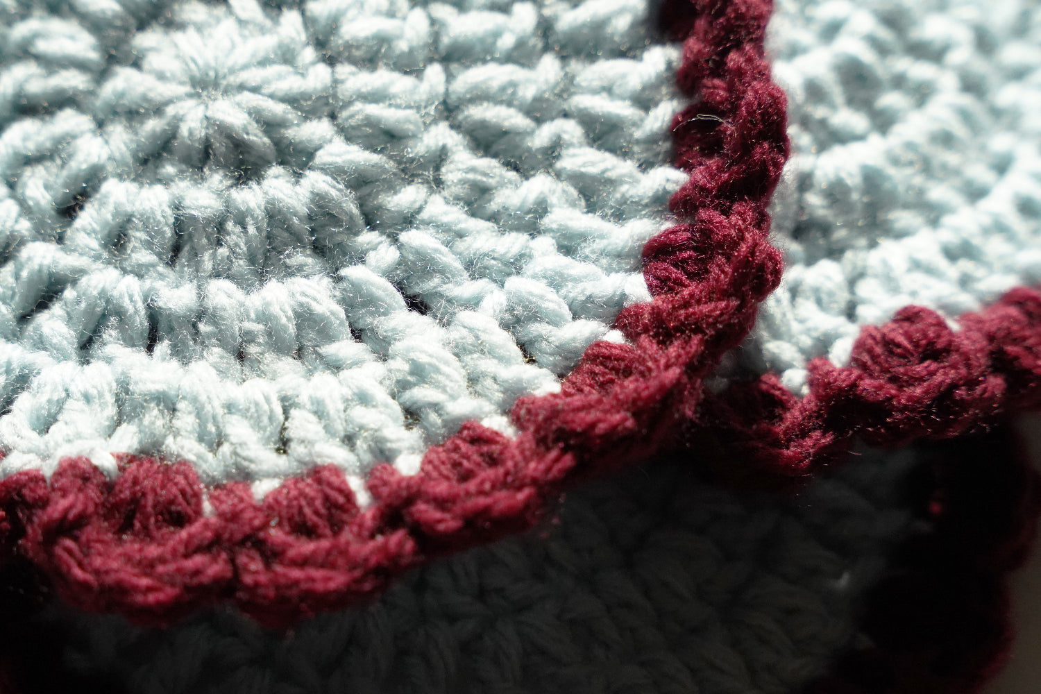 Close-up of a crocheted coaster with a red border on a white background