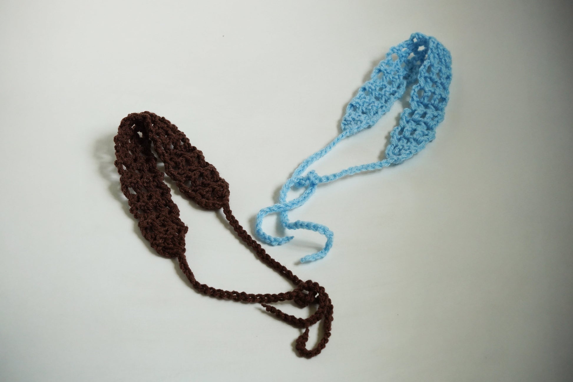 Two crocheted headbands, one brown and one blue, on a light gray background.