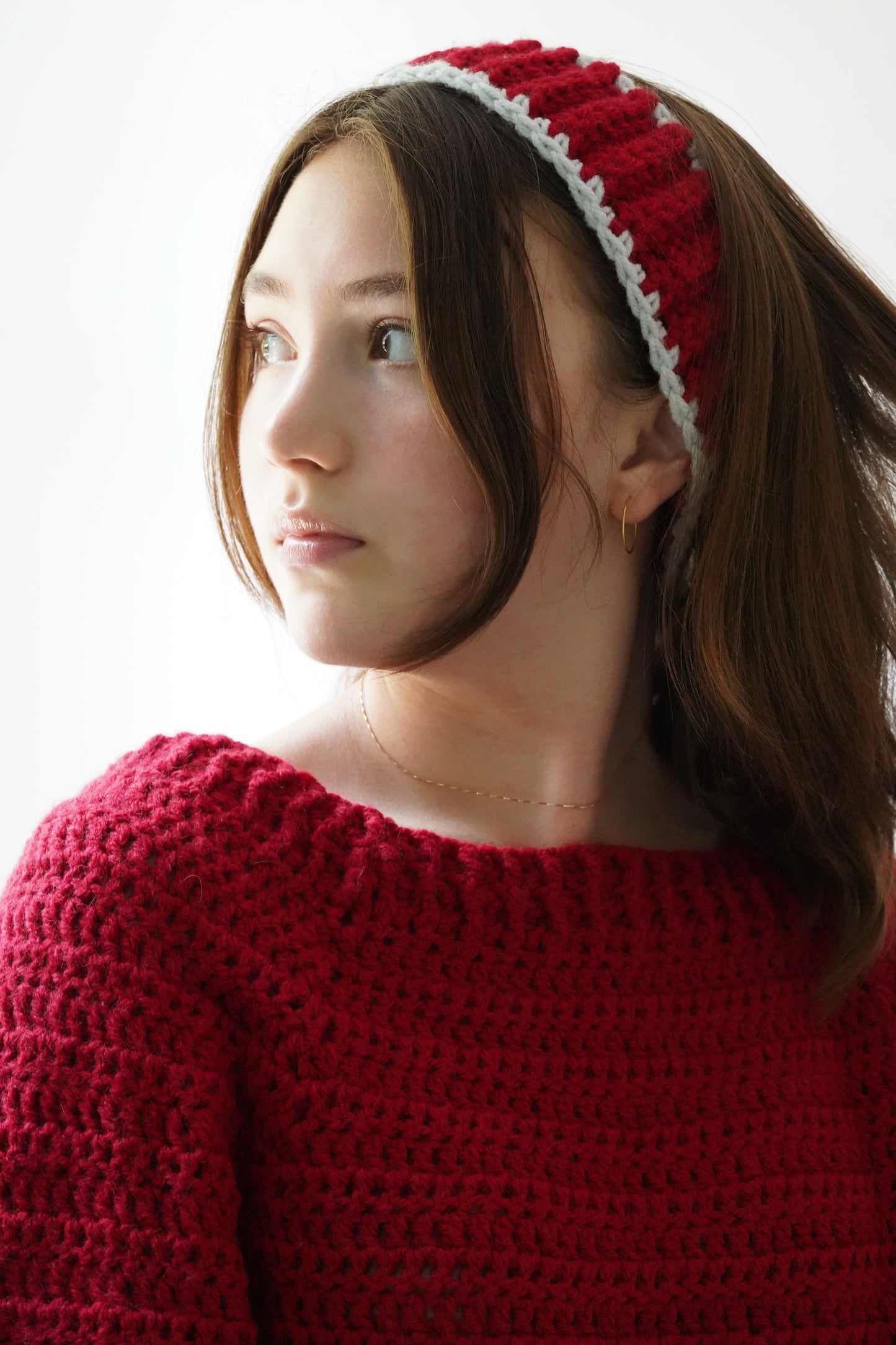 Woman wearing a red knitted headband and sweater against a white background