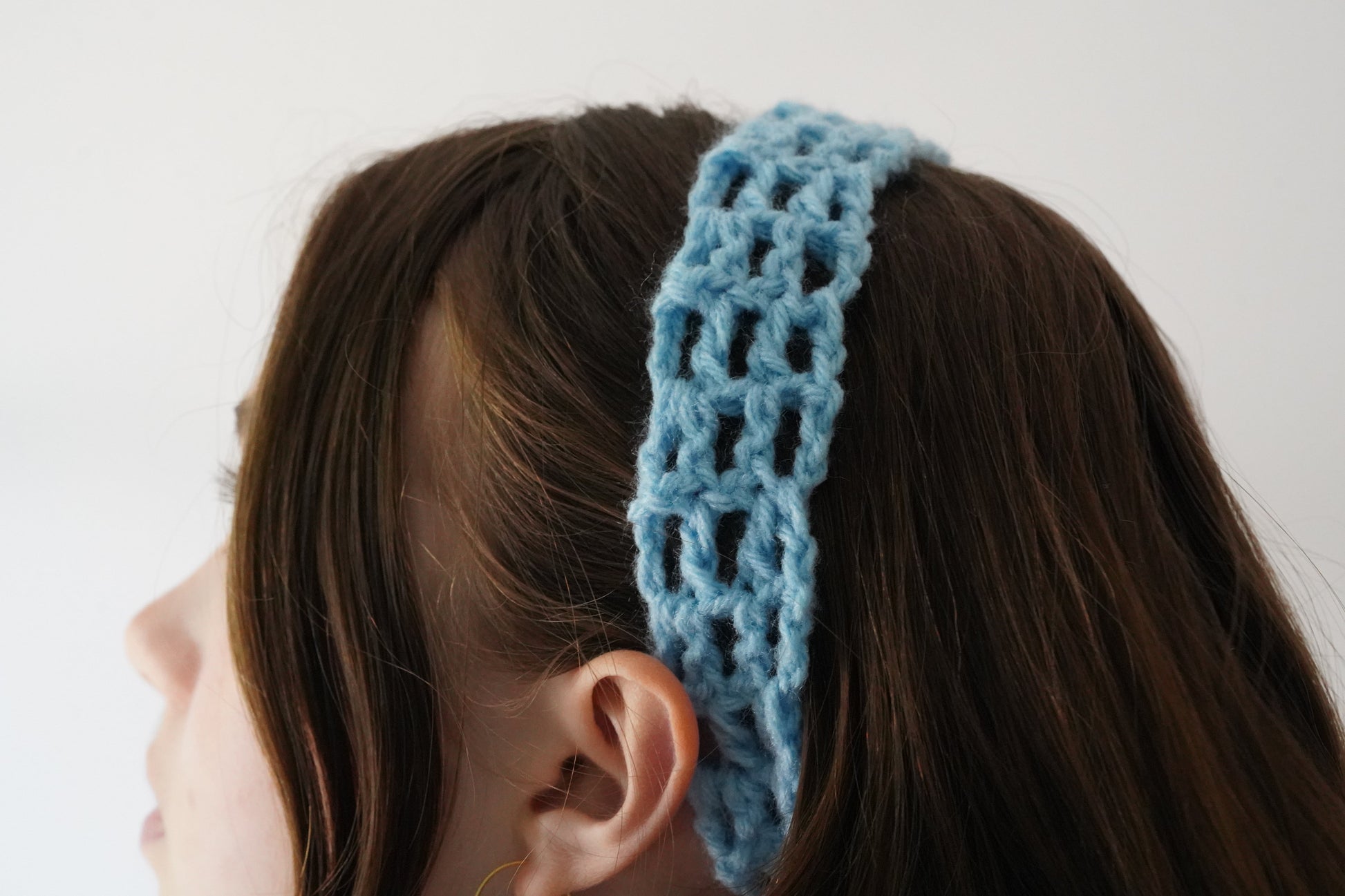 Blue knitted headband worn by a person with a plain background