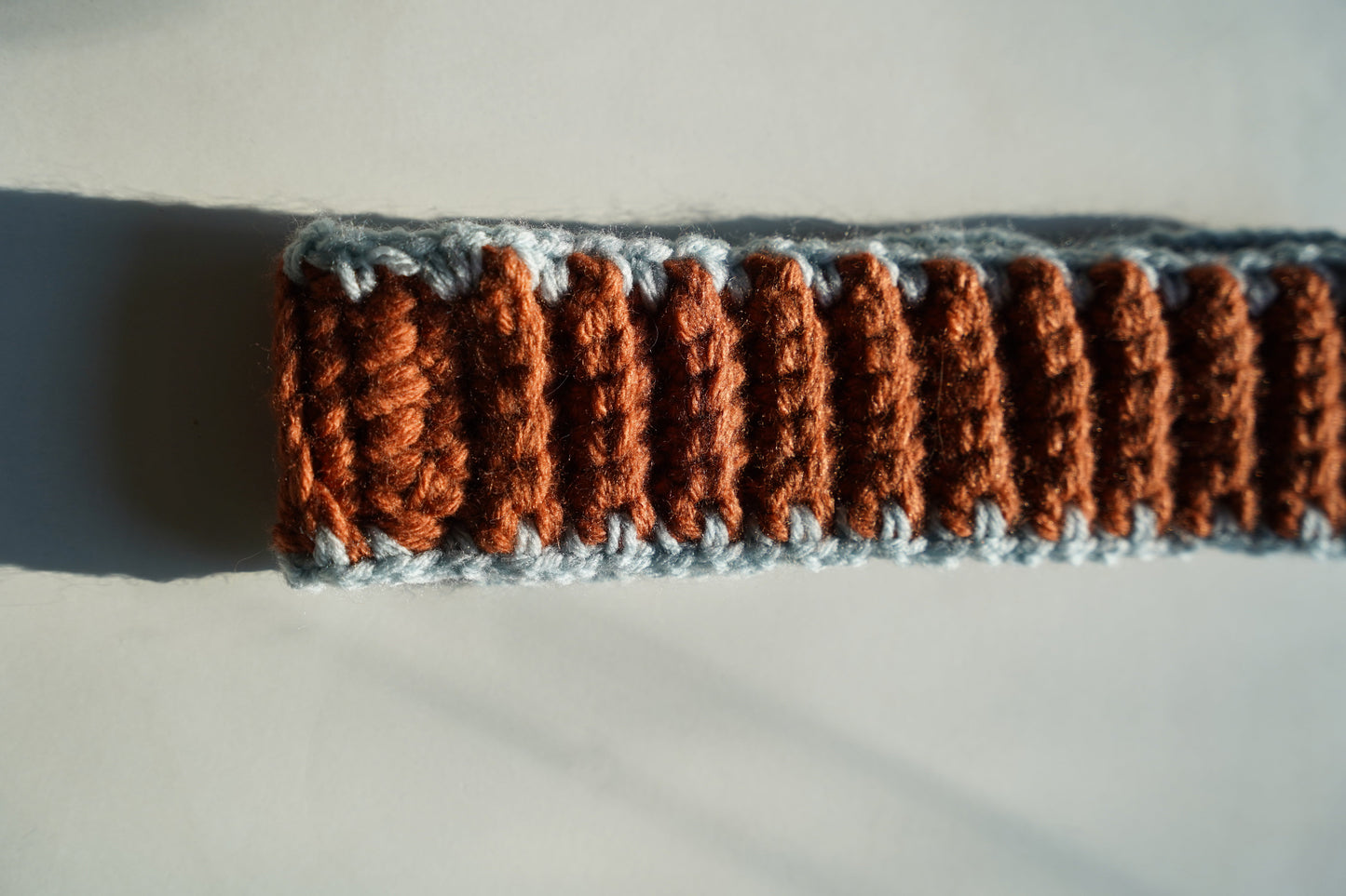 Close-up of a crocheted headband with brown and gray pattern on a light background