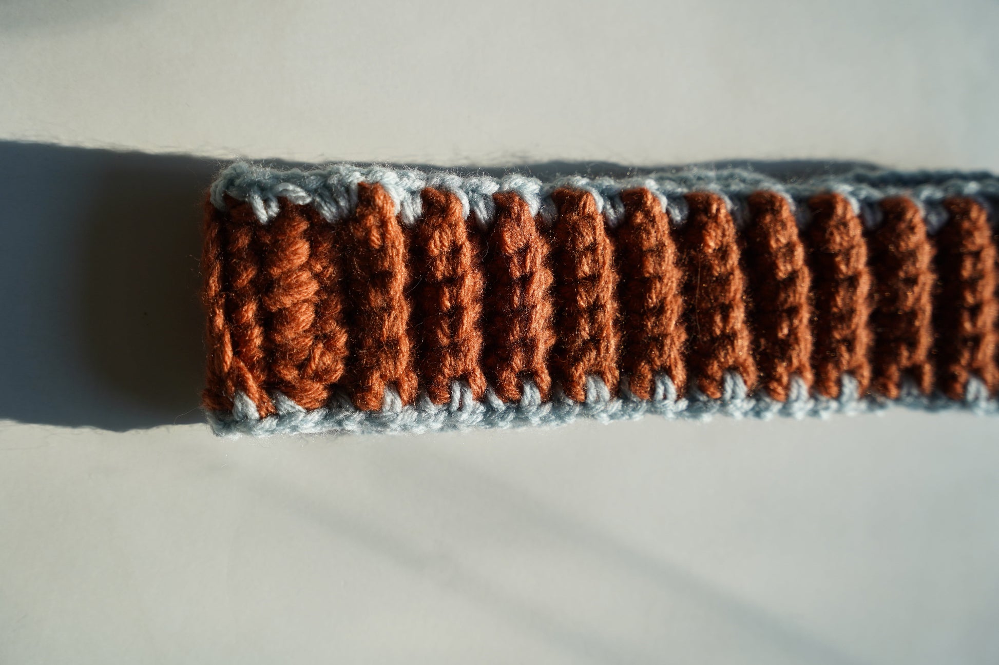 Close-up of a crocheted headband with brown and gray pattern on a light background