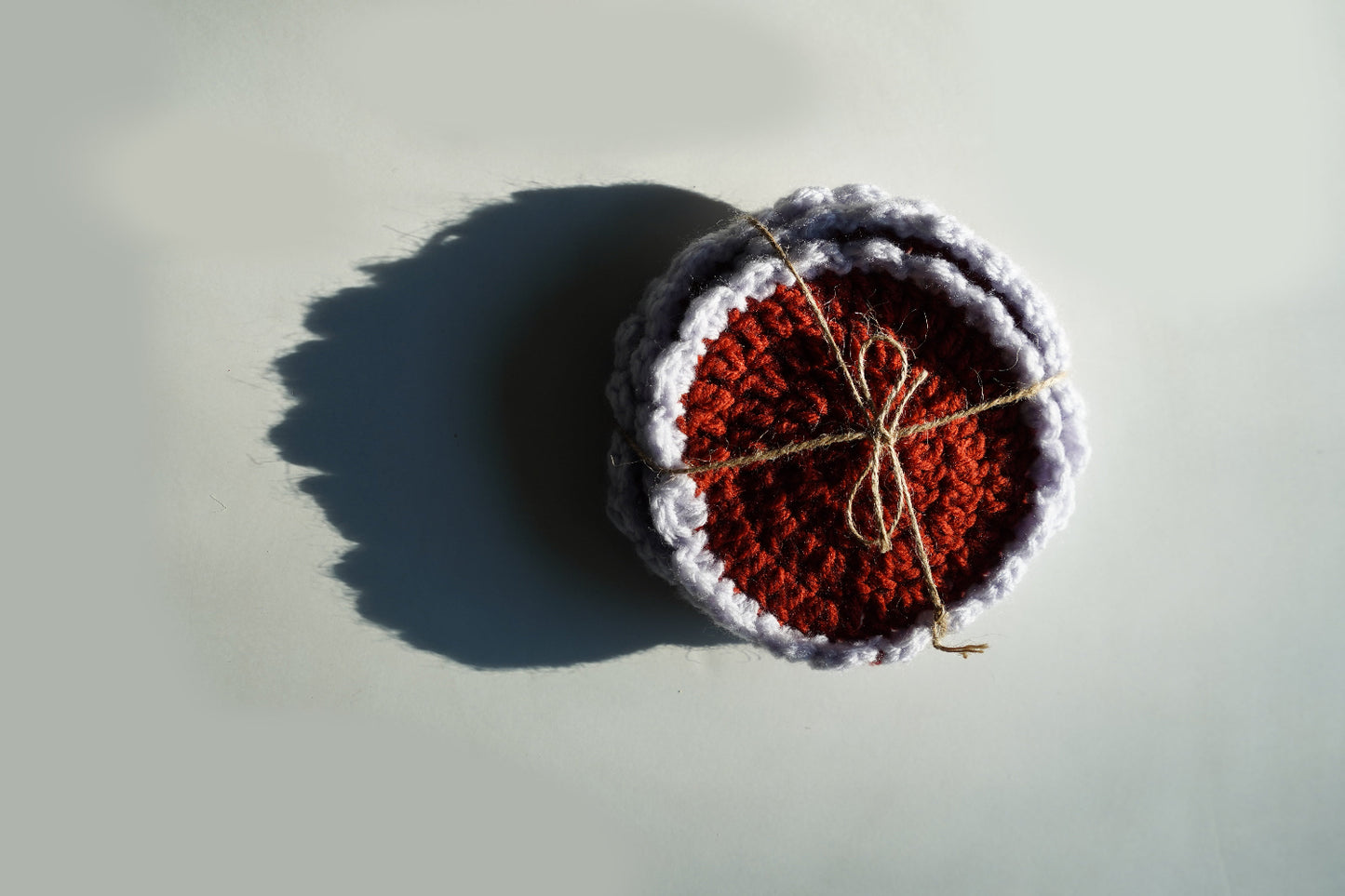 Crocheted coasters with red center and lilac border on a light gray background