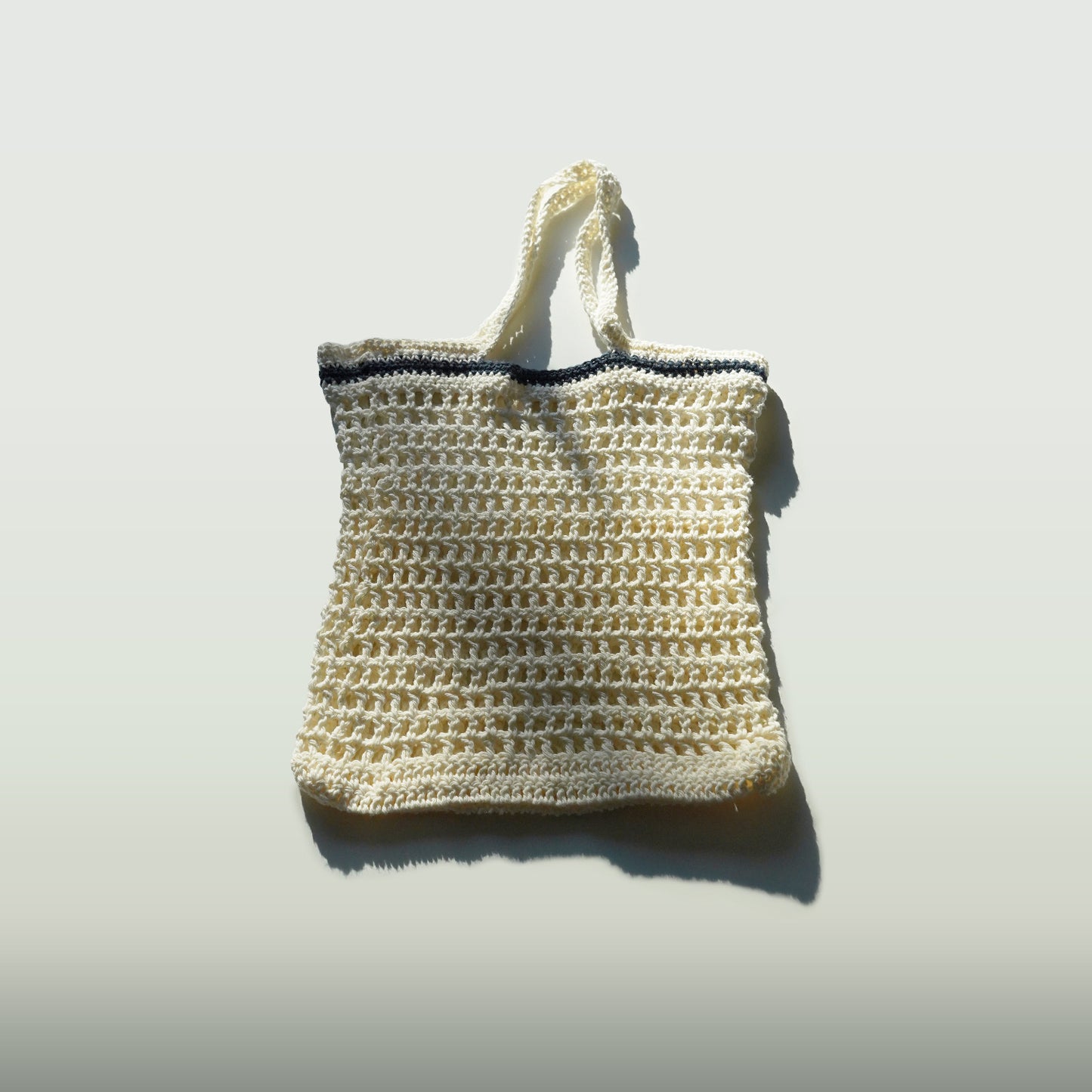 Handmade crochet bag with a navy blue stripe on a light gray background