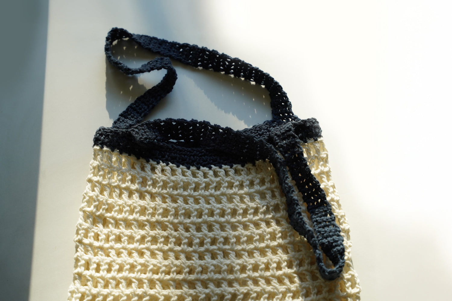 Handmade crochet bag with dark blue top and cream bottom on a white background