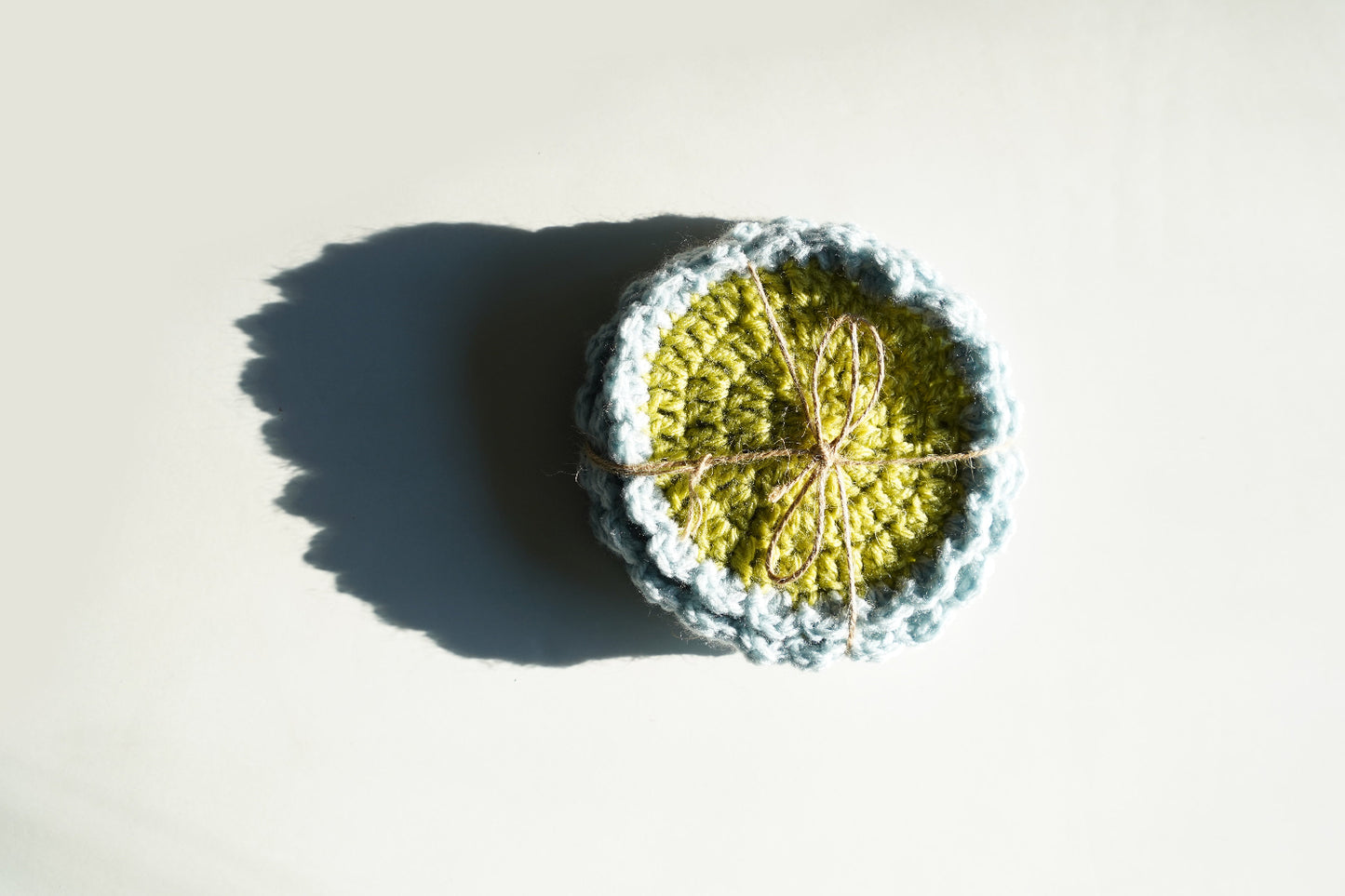 Crocheted coasters with green center and blue border on a light background