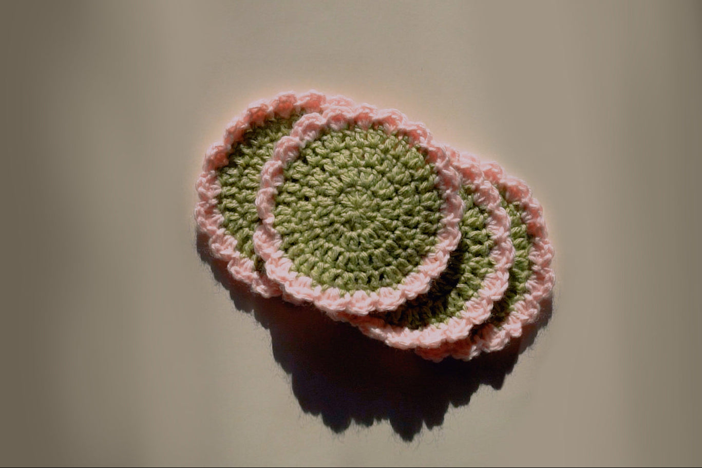 Four crocheted coasters with pink rims on a beige background