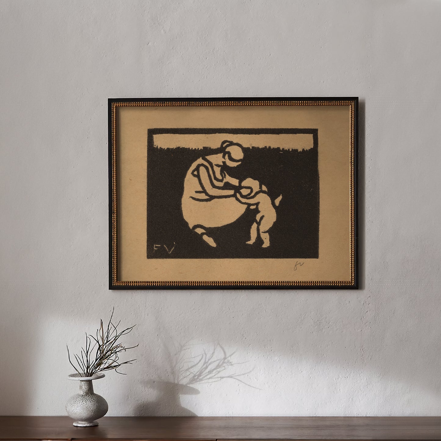 Framed artwork of a mother and child on a wall with a vase below.