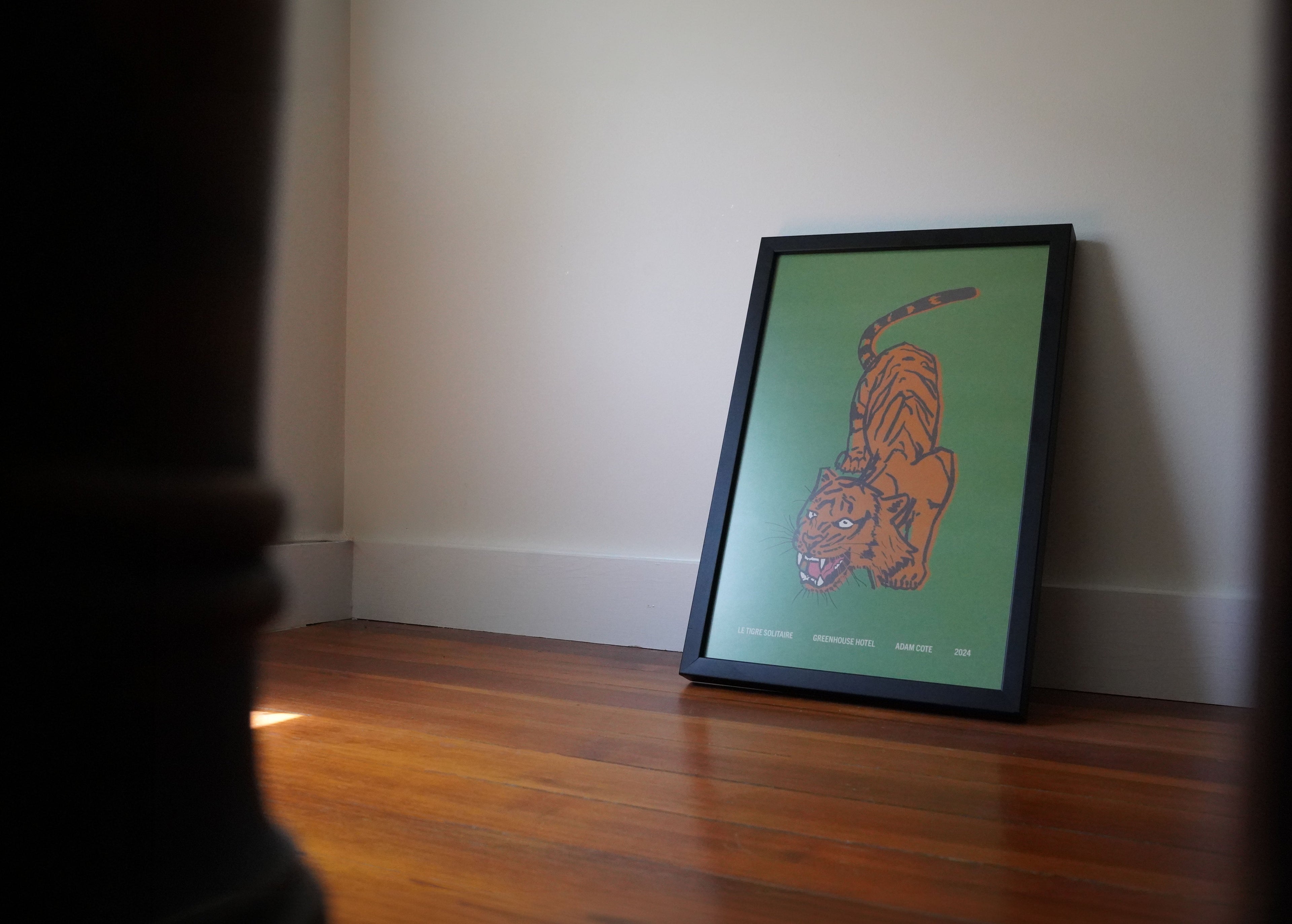Framed poster with a tiger design on a wooden floor against a white wall