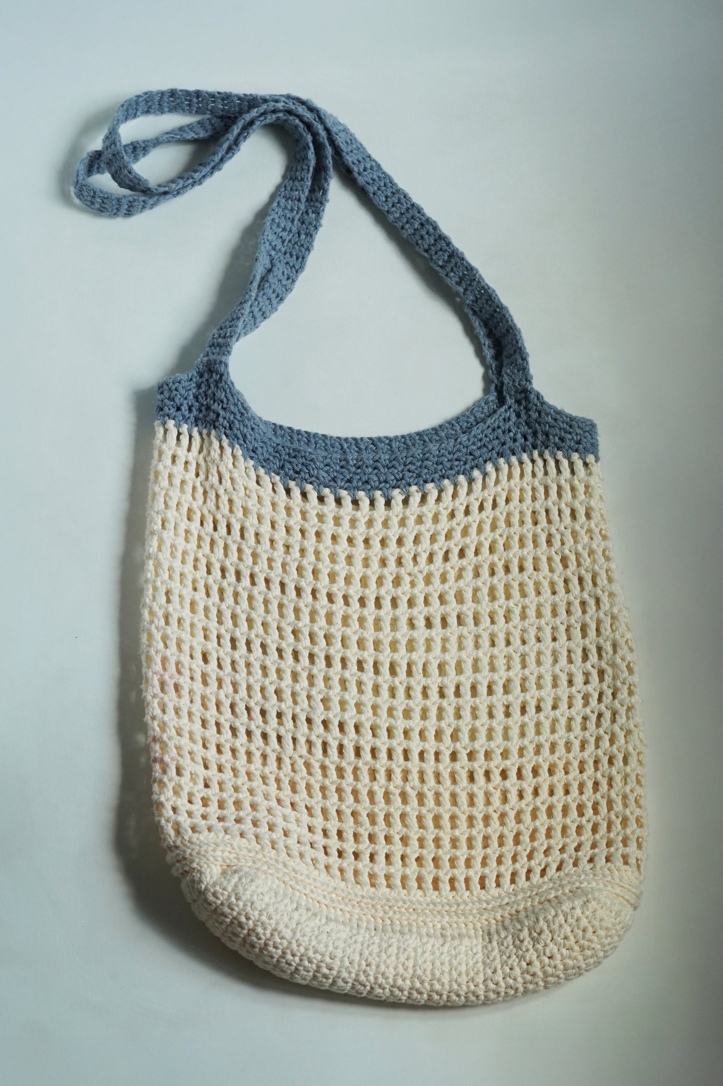 Crocheted bag with blue top section and beige bottom section on a light gray background